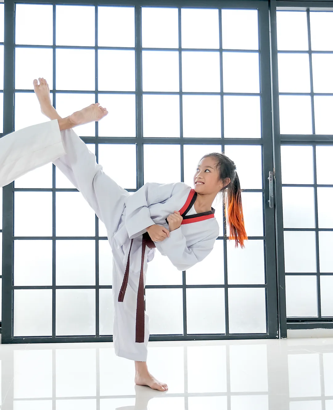 A girl in a white Taekwondo uniform lands a side kick on a target held by her instructor